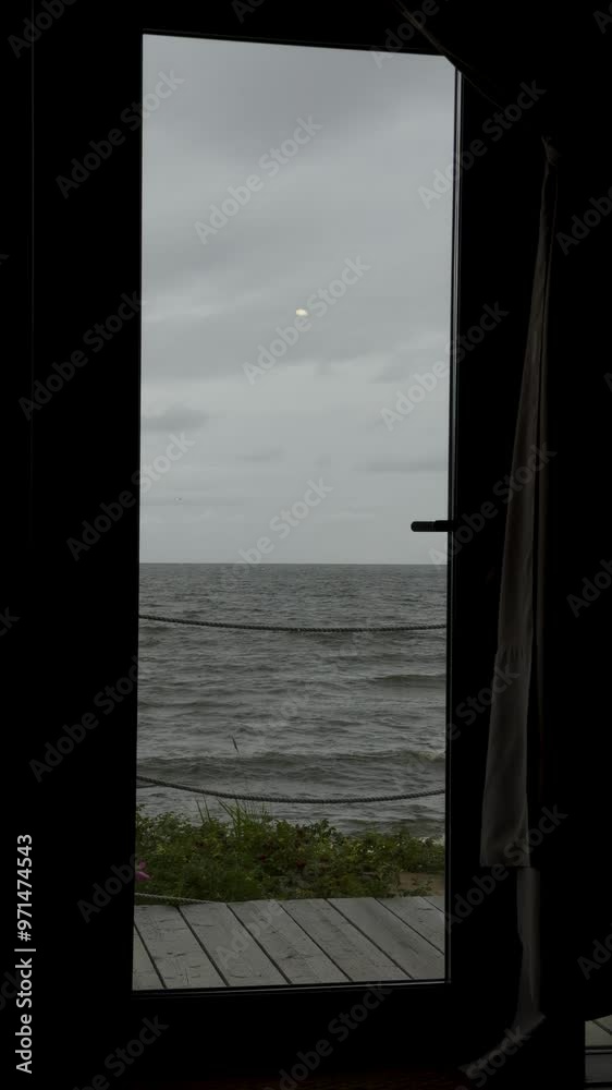 A serene view of the sea seen through an open doorway, with a cloudy sky above and gentle waves rolling onto the shore. The framing of the door and the rope fencing adds a cozy and intimate feel A serene view of the sea seen through an open doorway, with a cloudy sky above and gentle waves rolling onto the shore. The framing of the door and the rope fencing adds a cozy and intimate feel