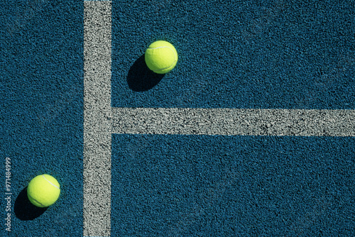 Yellow tennis ball with sunny shadow on blue tennis court with artificial covering. View from above. Sports background.