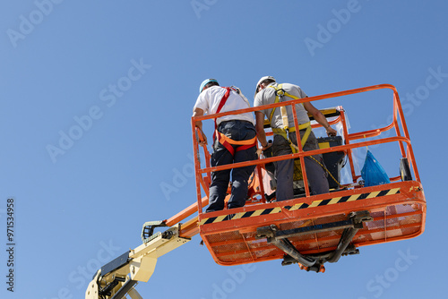 Cuadro en lienzo Low angle view of a Two workers on a cherry picker with safety equipment on a sunny day