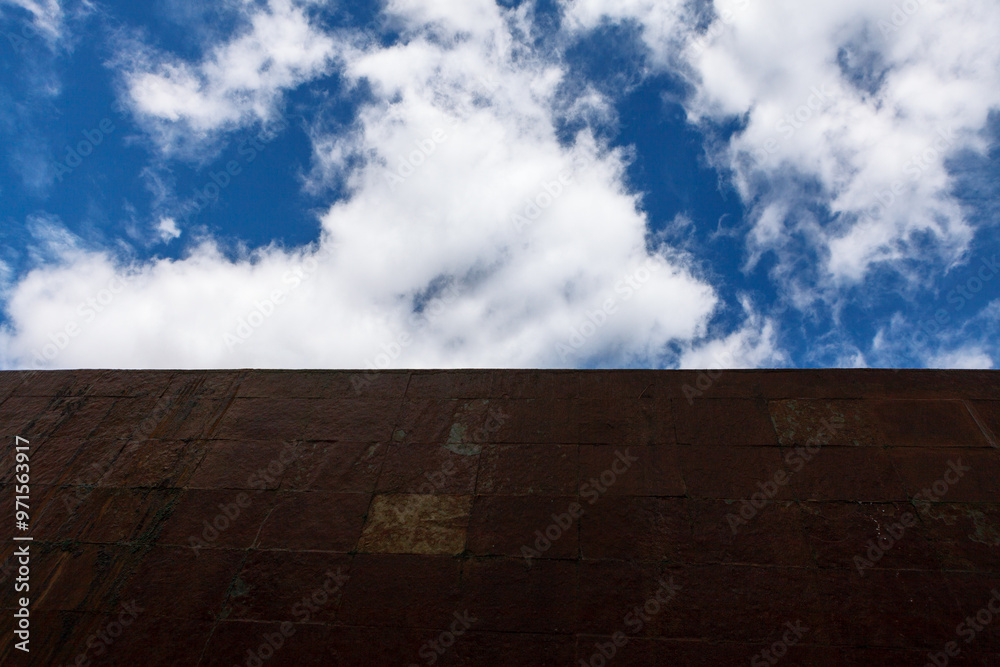 Blue sky over the brick wall. Serene view of the sky filled with fluffy clouds, captured from the ground