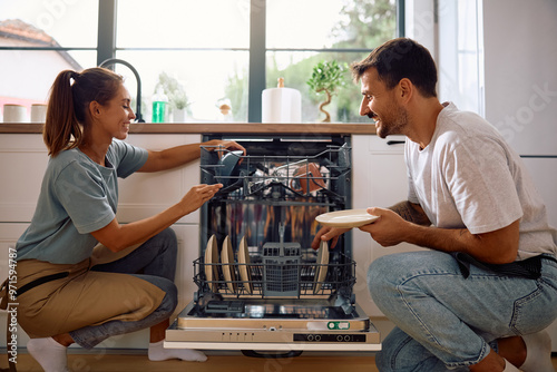 Young happy couple using dishwasher in  kitchen.