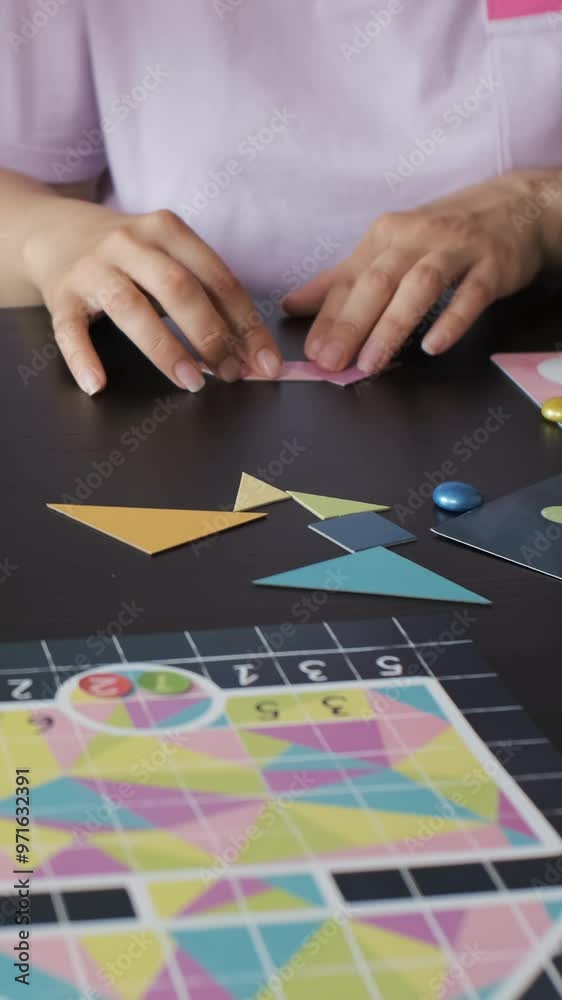 Vertical video. Young mother and her daughter playing a board game in the kitchen, connecting colorful geometric shapes of a tangram puzzle. Enjoying happy time together Vertical video. Young mother and her daughter playing a board game in the kitchen, connecting colorful geometric shapes of a tangram puzzle. Enjoying happy time together