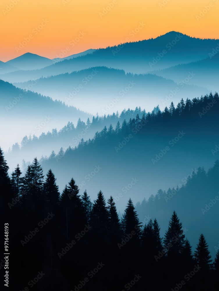 Obraz premium Serene mountain landscape at sunset, showcasing layered hills and misty forests beneath a vivid orange sky.