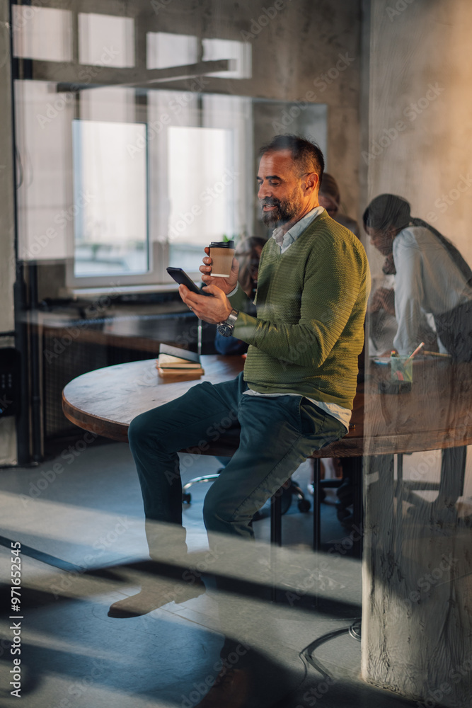View trough a glass of a mature businessman drinking coffee and using phone View trough a glass of a mature businessman drinking coffee and using phone