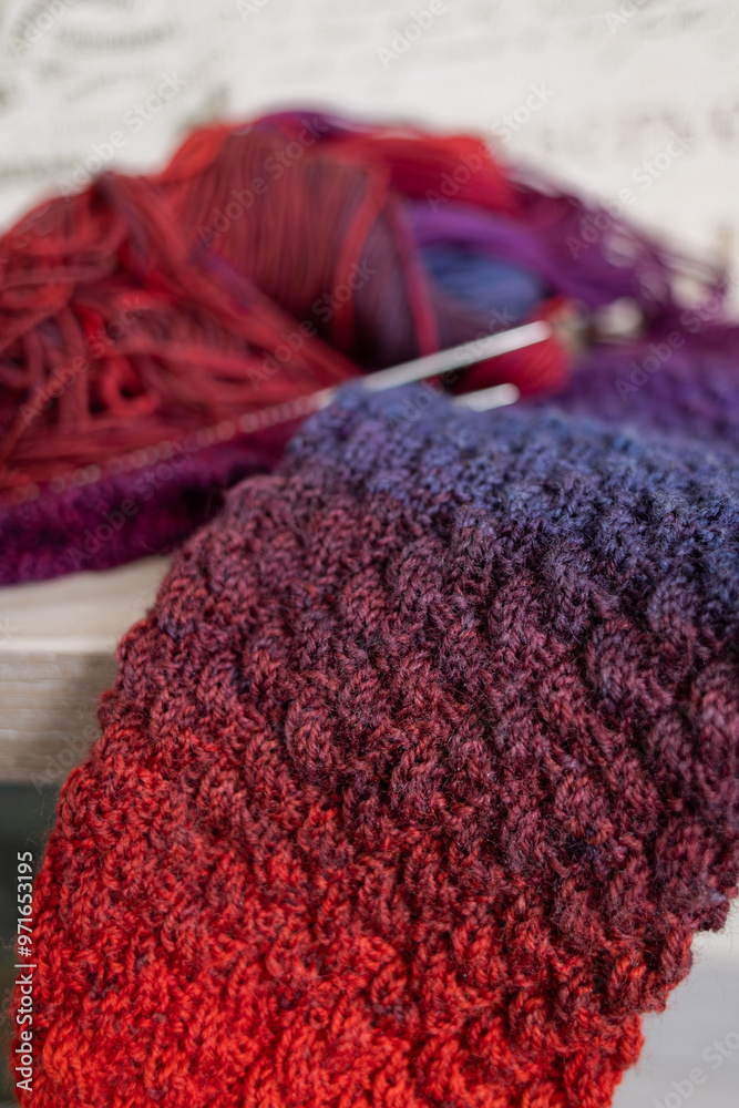 Fototapeta premium Knitted items. Self-made warm socks. Knitting pattern. Quality wool thread. Red-blue gradient. Cozy details. Home comfort. Colored yarn. Winter clothes. Christmas gift. Calm winter hobby. Wool socks.