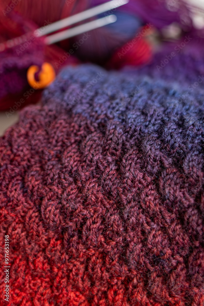 Fototapeta premium Knitted items. Self-made warm socks. Knitting pattern. Quality wool thread. Red-blue gradient. Cozy details. Home comfort. Colored yarn. Winter clothes. Christmas gift. Calm winter hobby. Wool socks.