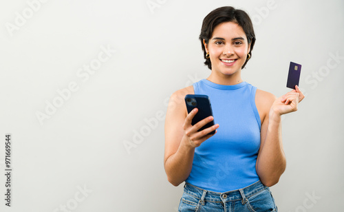 Latin woman holding a credit card and using her smartphone, embracing the ease of online banking