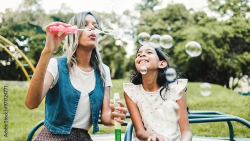 Family, Happy hispanic mother and daughter play blowing soap bubbles at park city. Latin mom having fun with child