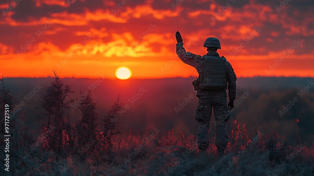 A soldier salutes the rising sun during a beautiful sunrise, while standing on a hill overlooking a forest.
