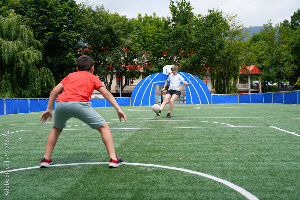 Obraz premium Mother and son playing soccer, as the boy practices blocking kicks on an outdoor field.