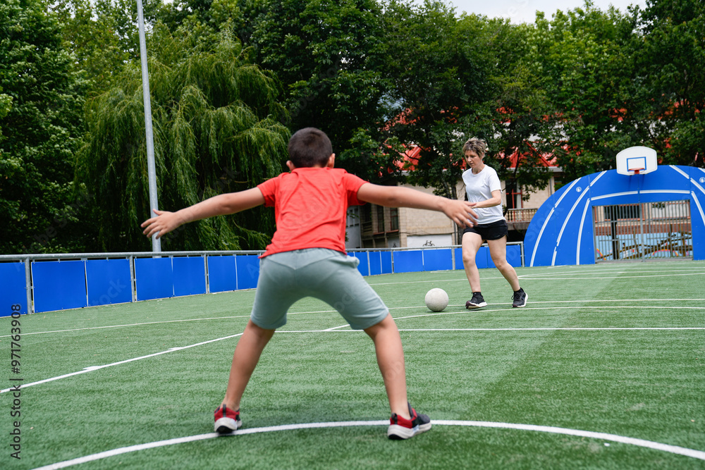 Obraz premium Mother playing soccer with her son, preparing to kick the ball on an outdoor field.