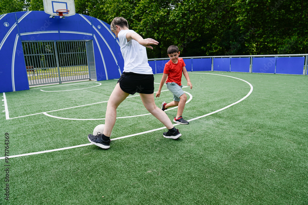 Fototapeta premium Mother teaches son soccer skills while playing together on a green field under the sun