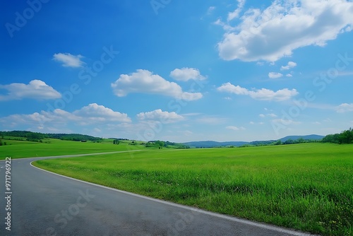 Empty asphalt road winding through lush green field and blue sky with clouds. Summer landscape with perspective and copy space