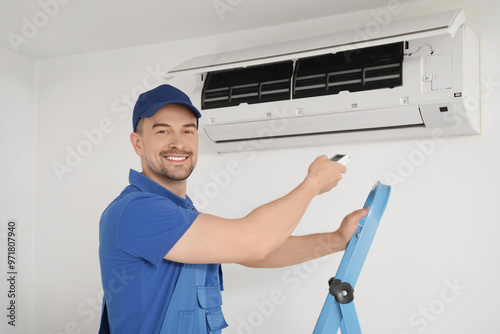 Male technician with remote control near air conditioner in room