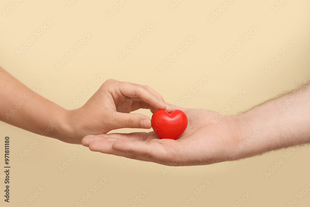 Hands of loving young couple with red heart on beige background Hands of loving young couple with red heart on beige background