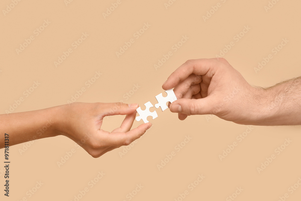 Hands of loving young couple with puzzle pieces on beige background Hands of loving young couple with puzzle pieces on beige background