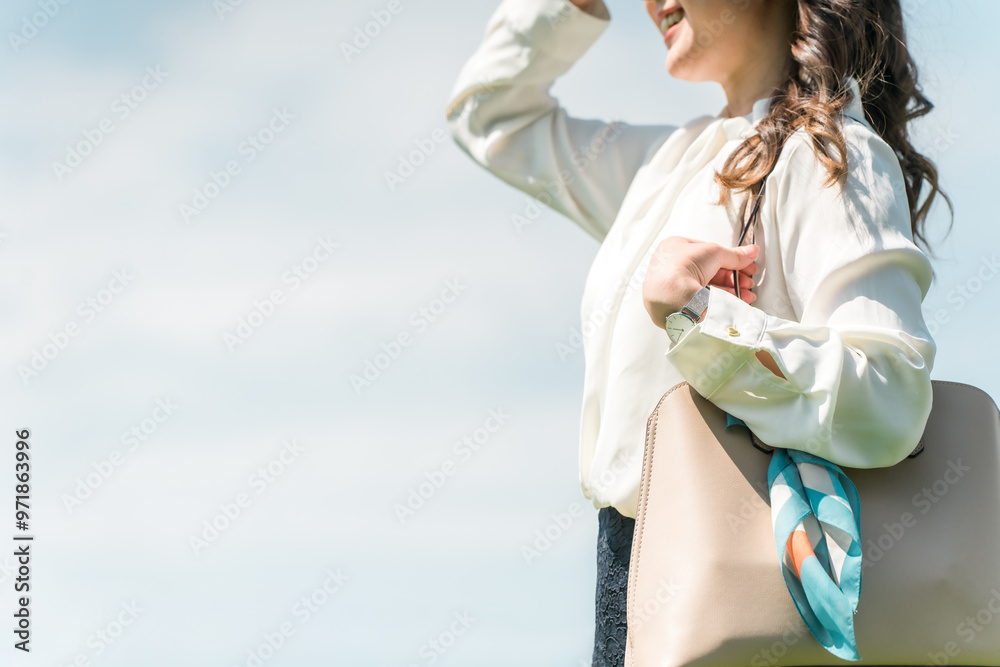 青空の下を歩く・出勤するビジネスウーマン（朝日・日光・日差し・眩しい）
