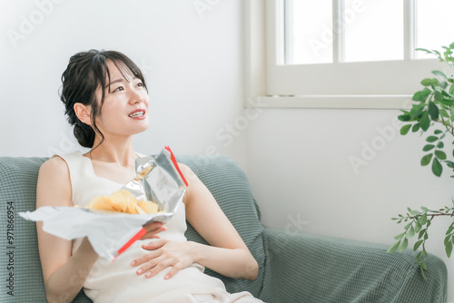 自宅のソファでポテトチップスを食べる若いアジア人女性（暴飲暴食・間食・高カロリー）
 photo