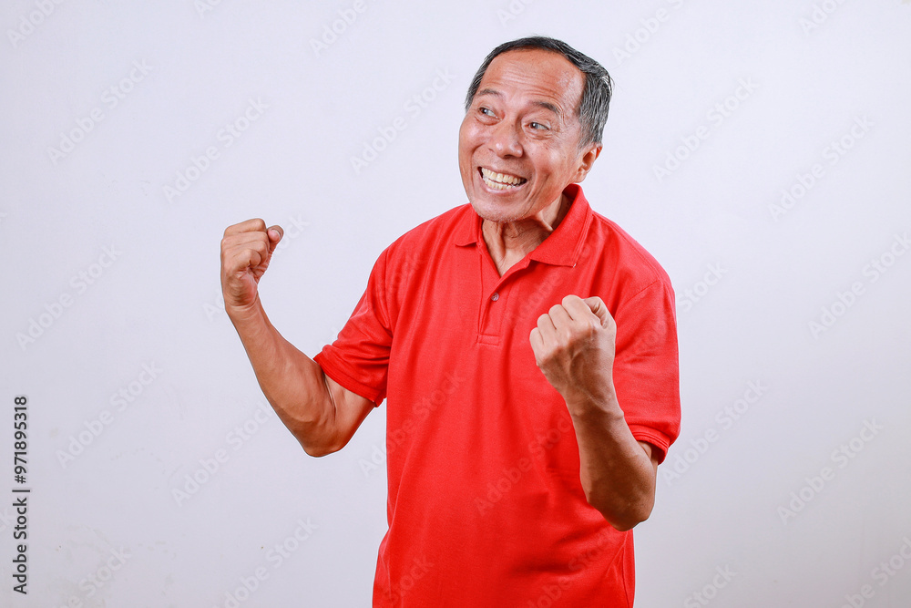 Fototapeta premium Senior Asian man in red t-shirt celebrating success with arms raised isolated on white background