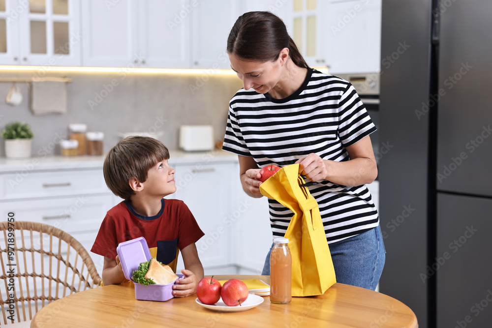 Fototapeta premium Mother and her cute son preparing lunch box with healthy food at wooden table in kitchen