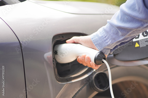 
Electric car charging at plug in charging station in a public car park. Renewable clean energy car for progressive eco awareness lifestyle concept.