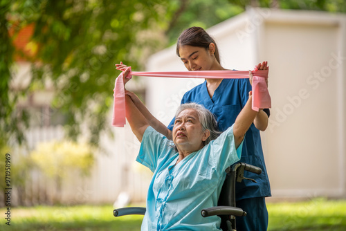 Healthcare or physical therapy nurse is helping elderly woman in performing a stretching or rehabilitation exercise with a resistance band caregiver individuals focused rehabilitation elderly concept.