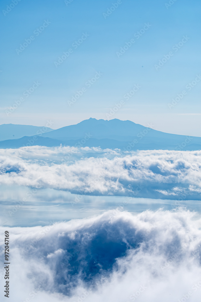 Naklejka premium 高所から見る雲と山の風景。眼下には立ち上るような雲、遠くには霞んだ山の稜線。