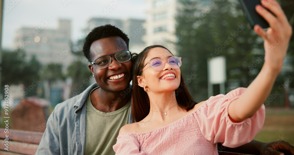 Smile, selfie and couple on bench in park with fun memory, social media post and interracial relationship. Love, photography and happy man with woman on romantic date with outdoor bonding together Smile, selfie and couple on bench in park with fun memory, social media post and interracial relationship. Love, photography and happy man with woman on romantic date with outdoor bonding together
