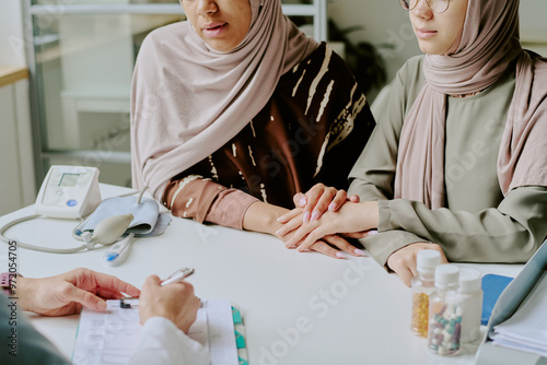 Canvas Print Two women wearing hijabs are discussing medical treatment with a doctor while si