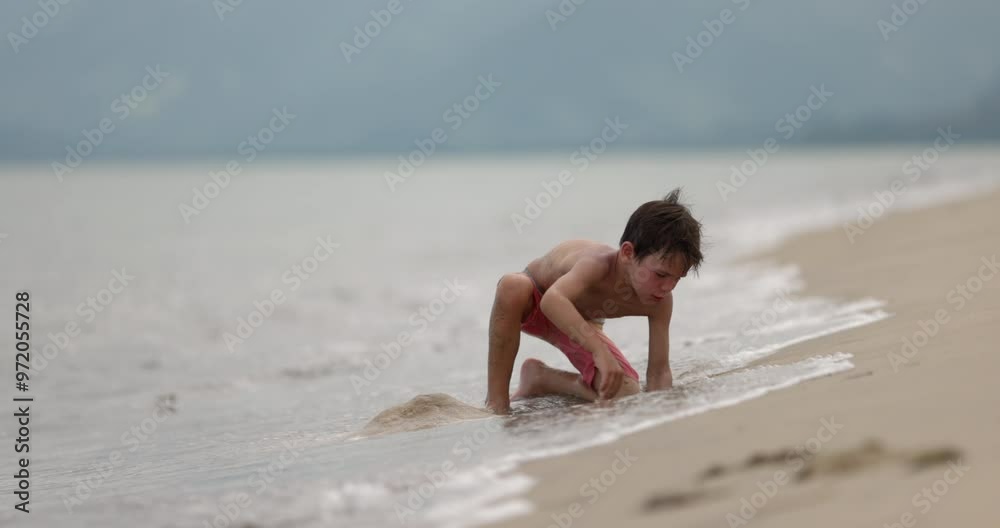 Young boy tries to scoop out water from hole digging in beach sand on tropical beach Young boy tries to scoop out water from hole digging in beach sand on tropical beach