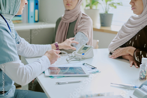Healthcare professional speaking with veiled patient about medical results while using stethoscope and blood pressure monitor during consultation in office setting