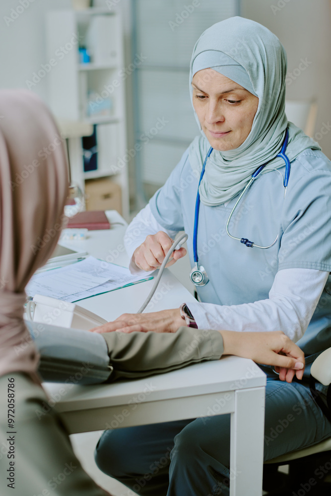 Obraz premium Medical professional wearing hijab attending to patient in modern clinic setting, performing checkup. Stethoscope and medical documents present, conveying professionalism and care