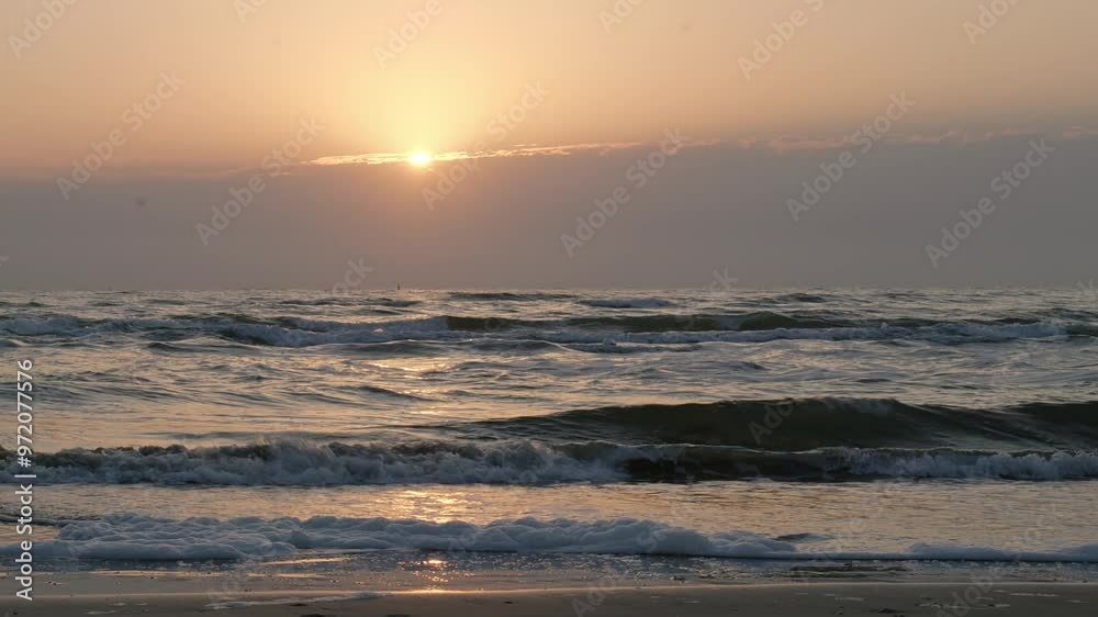 Gentle waves roll on a serene beach at sunrise with golden light reflecting on the water Gentle waves roll on a serene beach at sunrise with golden light reflecting on the water