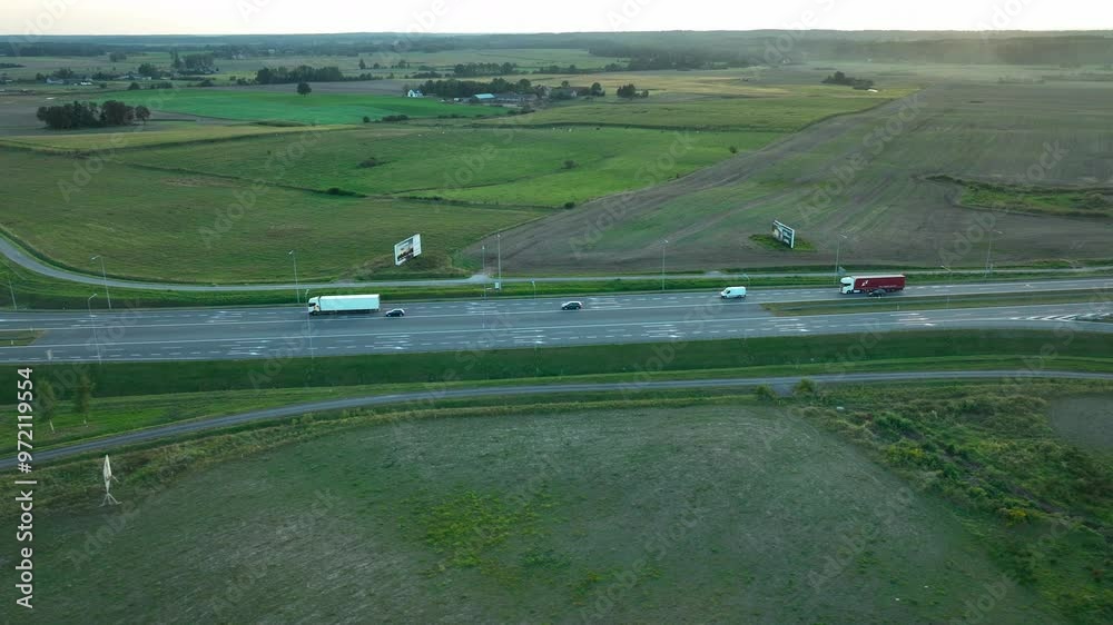 Aerial view of a highway with moving vehicles, surrounded by green fields and sparse vegetation, captured during the daytime Aerial view of a highway with moving vehicles, surrounded by green fields and sparse vegetation, captured during the daytime