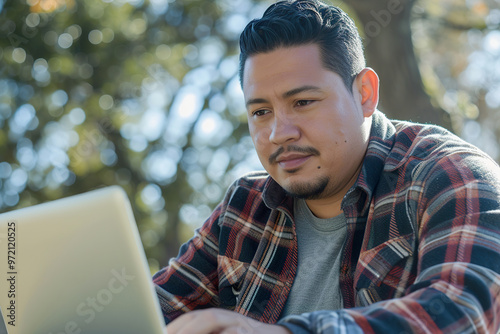 Hispanic man focuses on his laptop while seated on park bench, enjoying the outdoors