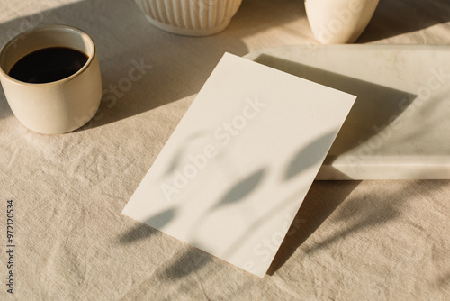 A blank piece of card on a table with ceramics, a cup of black coffee in sunlight.