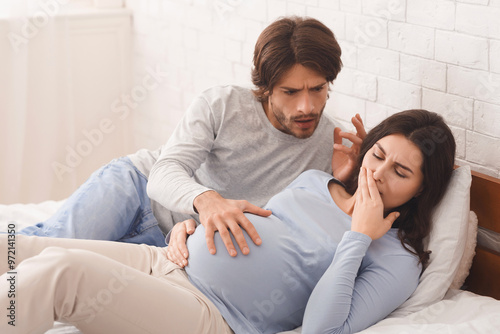 Pregnancy and morning sickness concept. Worried husband soothing his pregnant wife suffering from nausea while lying together in bed photo