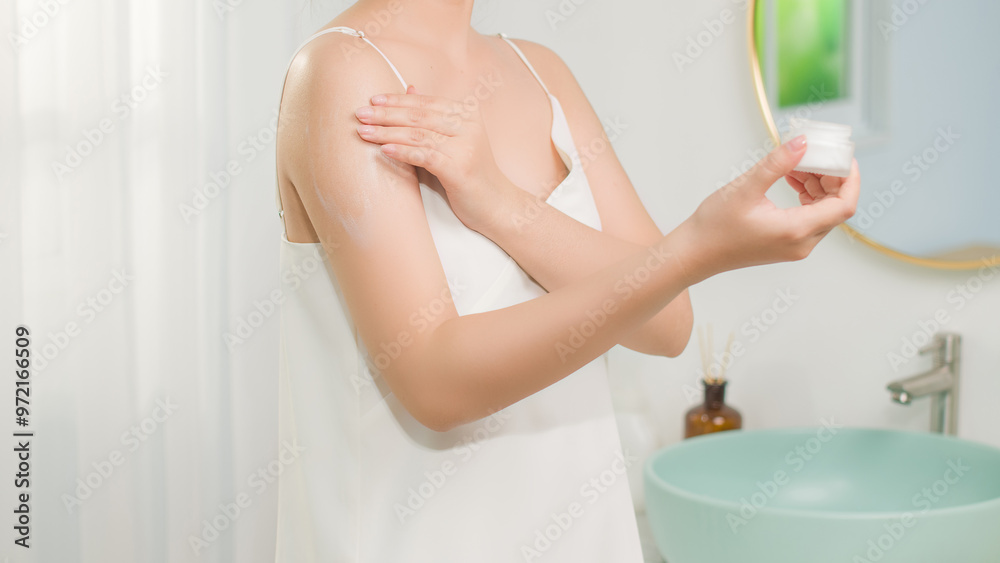 Lifestyle photo in bathroom with white dress female model, who is spreading lotion on skin after shower. Front view, blank space for designing and advertising Lifestyle photo in bathroom with white dress female model, who is spreading lotion on skin after shower. Front view, blank space for designing and advertising