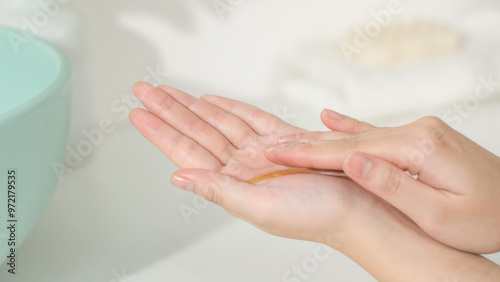 High angle close-up shot of two hands with serum spread evenly in the palms, over blurred background. The photo of bathroom theme, space for text