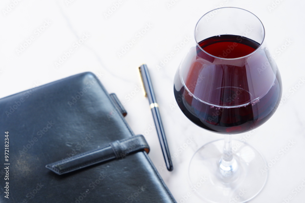 Φωτογραφία 赤ワインを飲みながら、黒い革のシステム手帳に日記をつけているイメージ