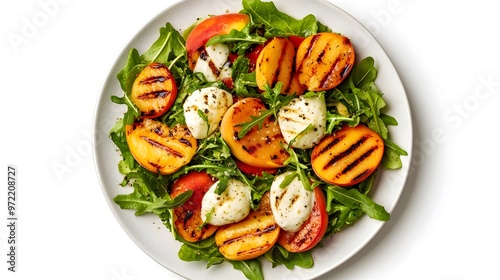 Grilled peach and mozzarella salad with arugula and tomatoes on white plate