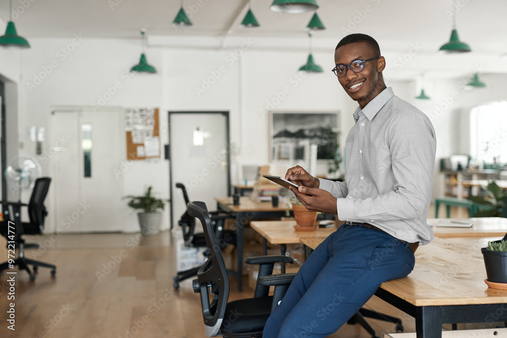 African businessman smiling while using a tablet at his office desk African businessman smiling while using a tablet at his office desk