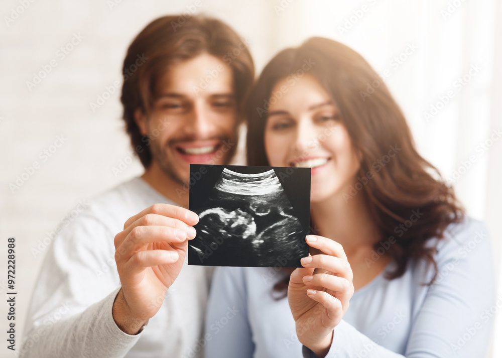Happy young couple looking at sonography picture of their baby, selective focus on ultrasound scan in their hands Happy young couple looking at sonography picture of their baby, selective focus on ultrasound scan in their hands
