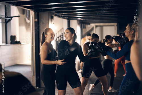 Young female coach helping a woman wearing boxing gloves laughing together while doing a punching workout during a boxing class in a gym
