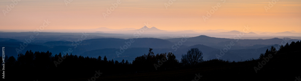 A breathtaking silhouette of twin peaks of Bezdez rises above a hilly landscape as the sun sets, casting warm hues over a tranquil Czechia panorama, surrounded by lush forests. A breathtaking silhouette of twin peaks of Bezdez rises above a hilly landscape as the sun sets, casting warm hues over a tranquil Czechia panorama, surrounded by lush forests.