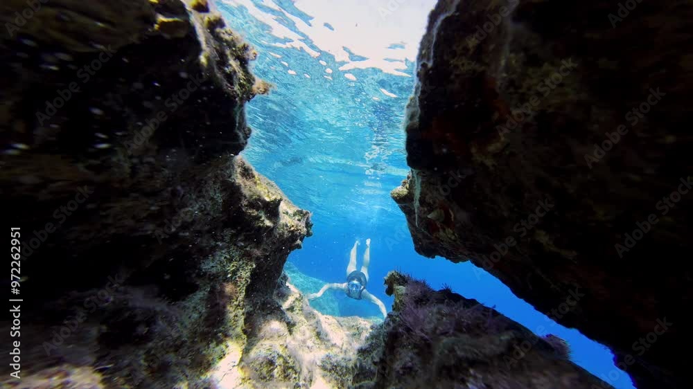 A beautiful girl in glasses swims under water between reefs in the sea. Active recreation, snorkeling in the ocean, exploring the underwater world. High quality 4k footage