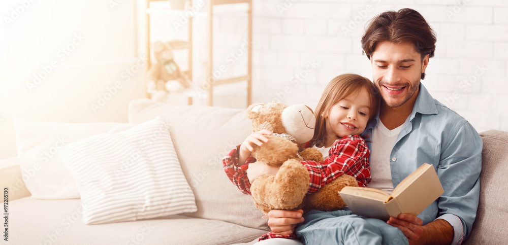 Daddy and daughter reading funny stories together at home, sitting on sofa in living room, free space Daddy and daughter reading funny stories together at home, sitting on sofa in living room, free space