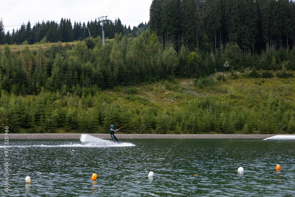 A person water skiing on a lake surrounded by forests on a cloudy afternoon A person water skiing on a lake surrounded by forests on a cloudy afternoon