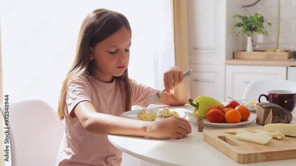 Little cute Caucasian girl with brown hair eating breakfast with eggs at table in kitchen starting morning with healthy meal enjoying delicious meal at home Little cute Caucasian girl with brown hair eating breakfast with eggs at table in kitchen starting morning with healthy meal enjoying delicious meal at home