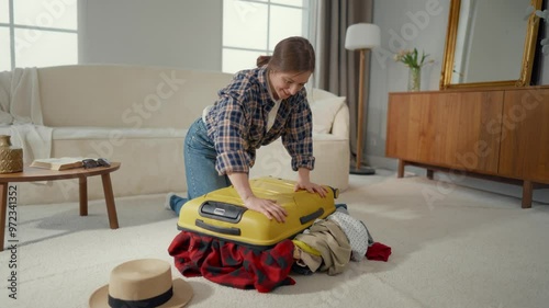 Big suitcase for summer voyage, woman trying to close overloaded bag at home. Traveling and tourism, funny young lady packing clothes for weekend in seacoast, too many gowns, excess baggage, removal